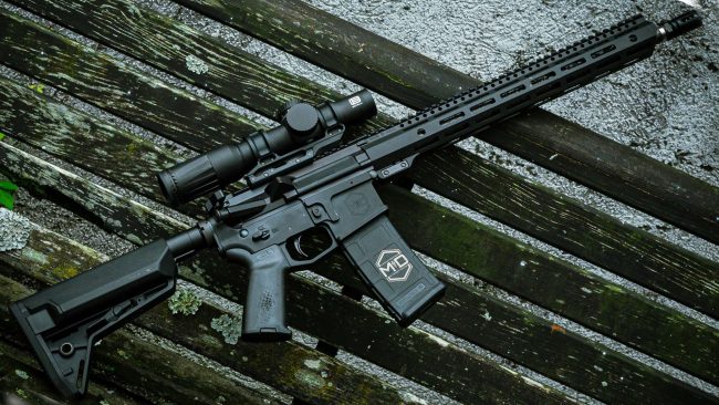 SOIDC DOC AR15 with scope leaned against wood bench